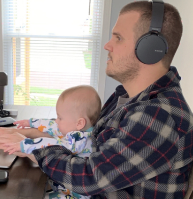 Blake, a member of the Rx Savings Solutions team, working from home, wearing headphones while his infant child sits on his lap.