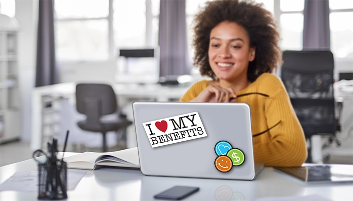 A woman works on her laptop and there's a sticker on the top of her laptop that says "I love my benefits"
